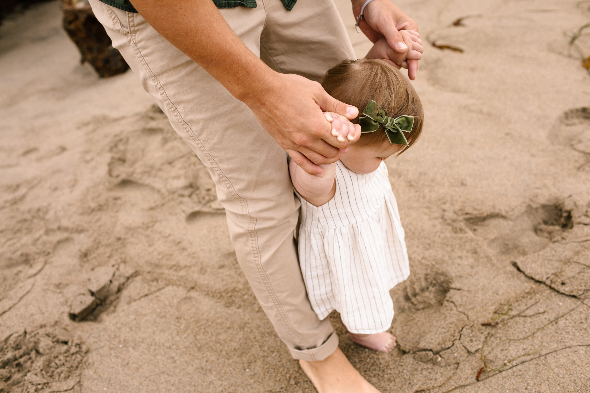 baby walking on sand holding dad's hand